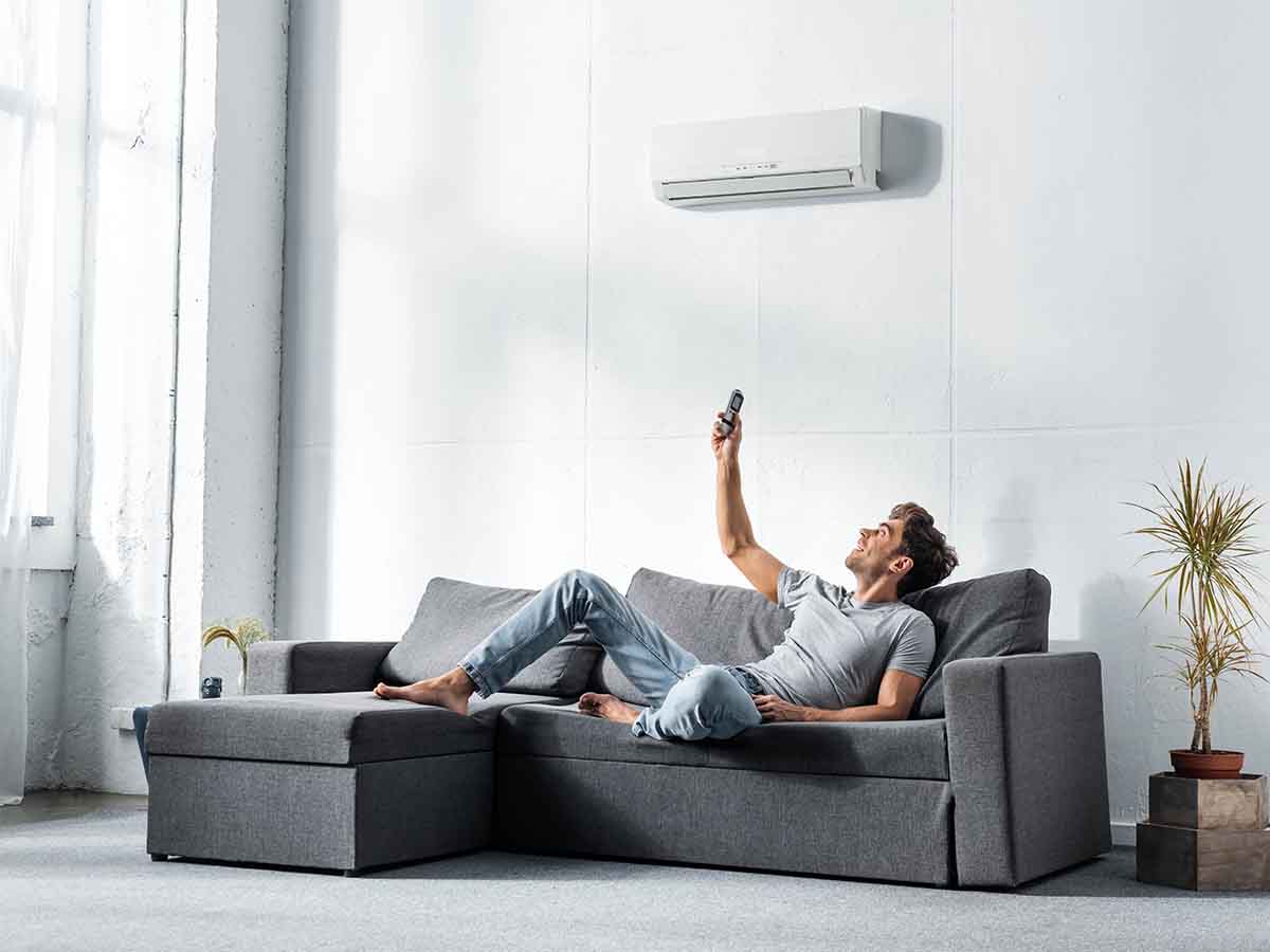 Handsome-man-lying-on-sofa-and-switching-on-mini-split-air-conditioner